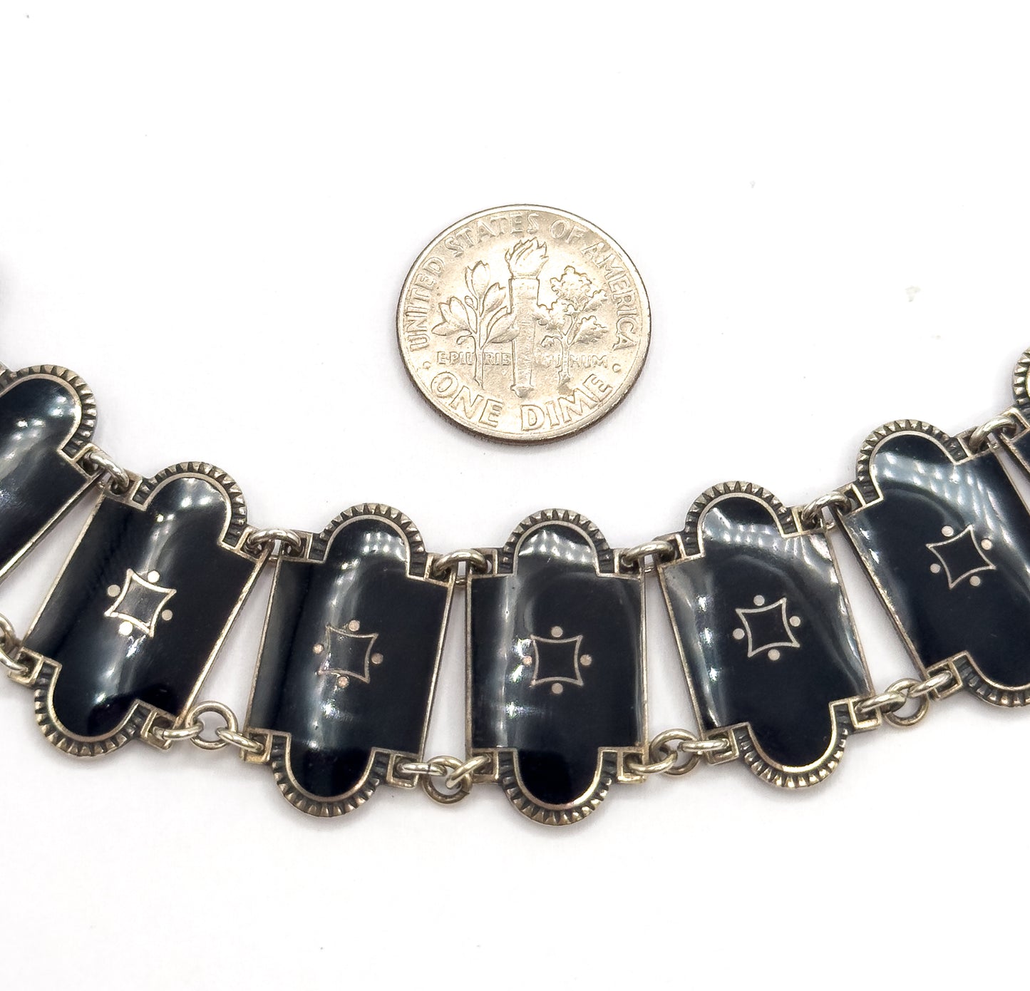 A dime rests above the row of enamel stations for scale, each link a little wider than the coin, with the small four-pointed star motifs and double jump rings clearly visible.