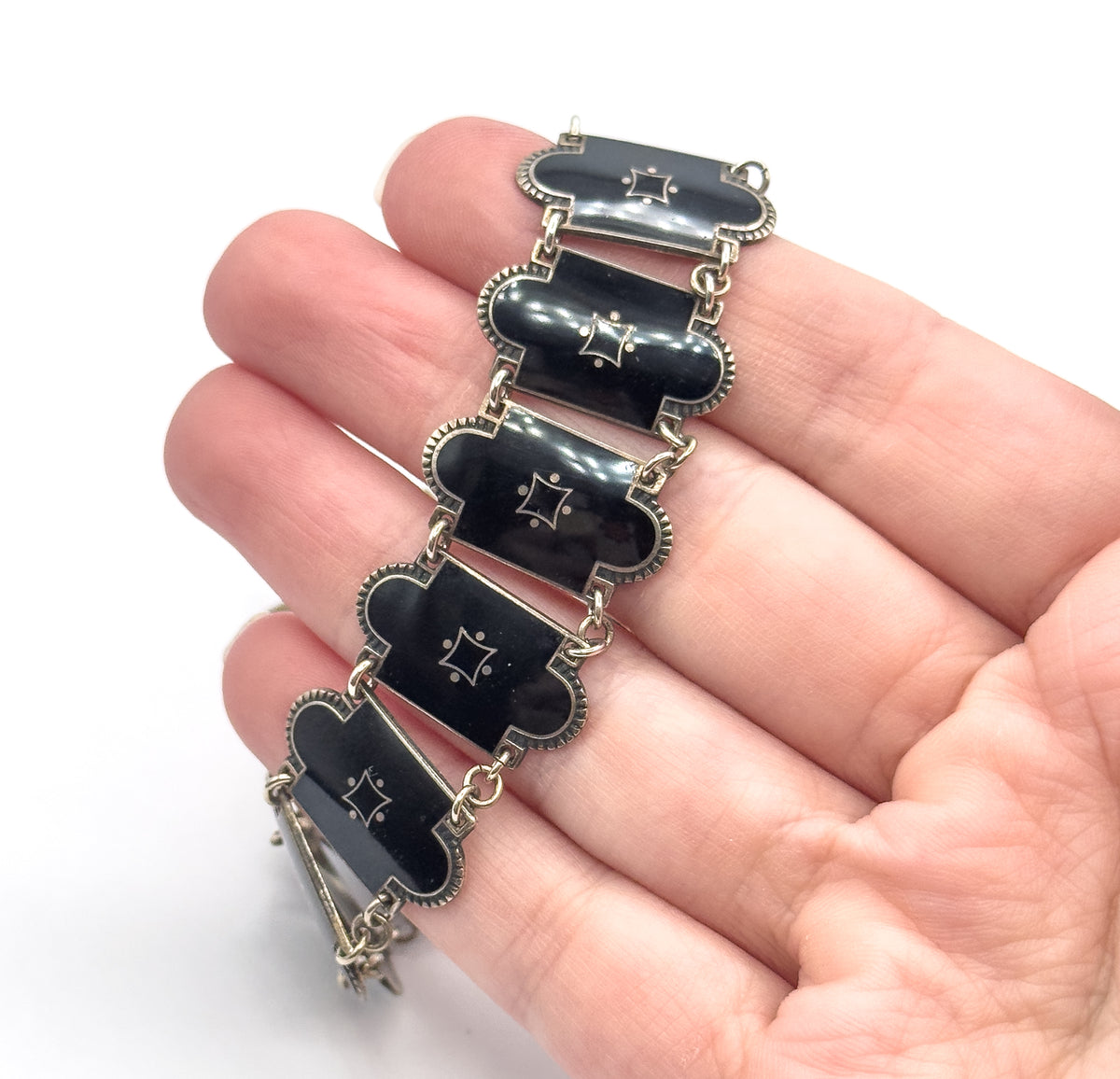 Five elongated black enamel links lie across the fingers of an open palm, each with a small four-pointed star motif and beaded silver border, the hand showing how narrow they are.