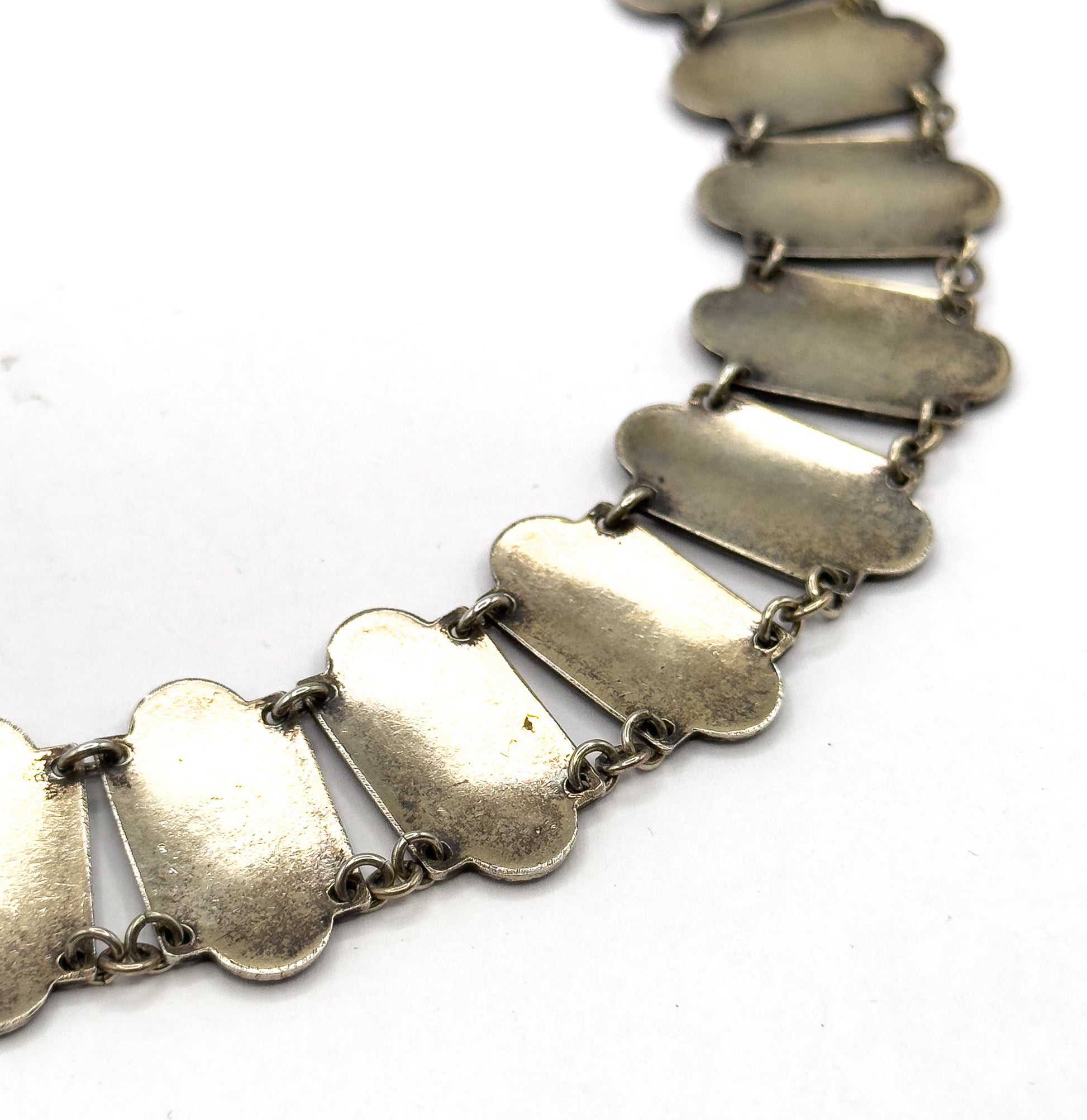 The reverse side of the necklace curves across a white background, showing the plain undersides of the elongated links and the small round jump rings joining each one.