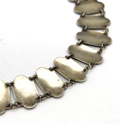 The reverse side of the necklace curves across a white background, showing the plain undersides of the elongated links and the small round jump rings joining each one.