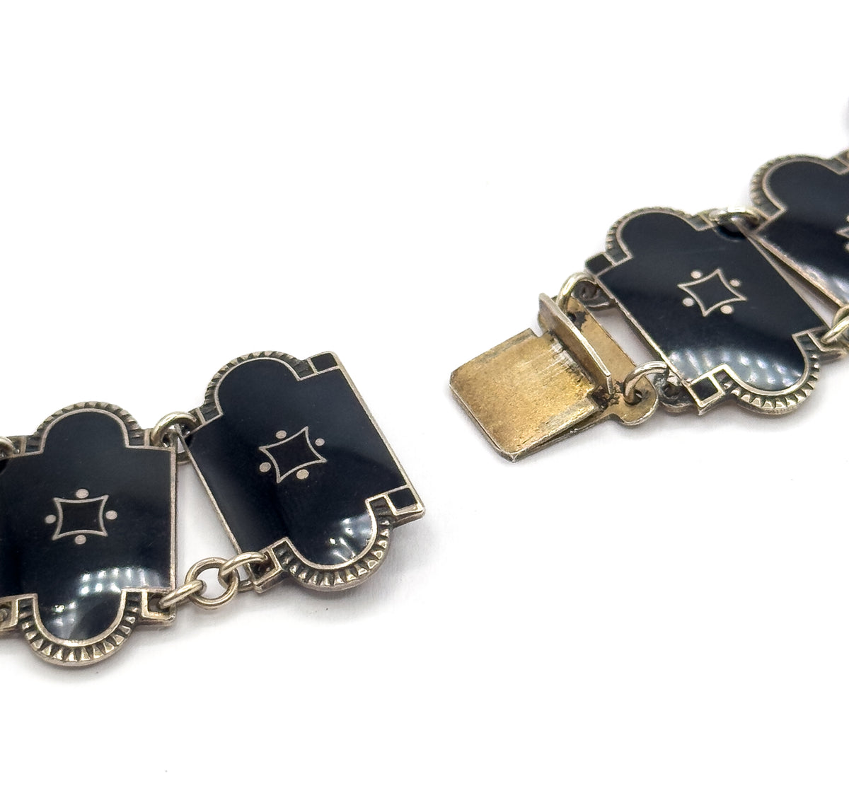 The clasp shown open from the front, its flat tongue extending free at the left while the black enamel links with star motifs and scalloped borders curve away on both sides.