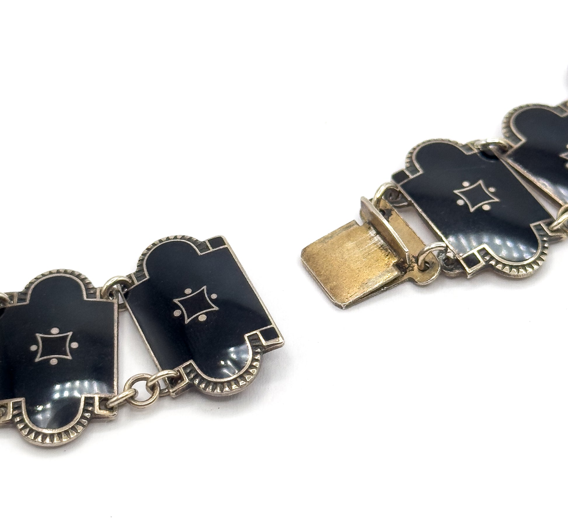 The clasp shown open from the front, its flat tongue extending free at the left while the black enamel links with star motifs and scalloped borders curve away on both sides.