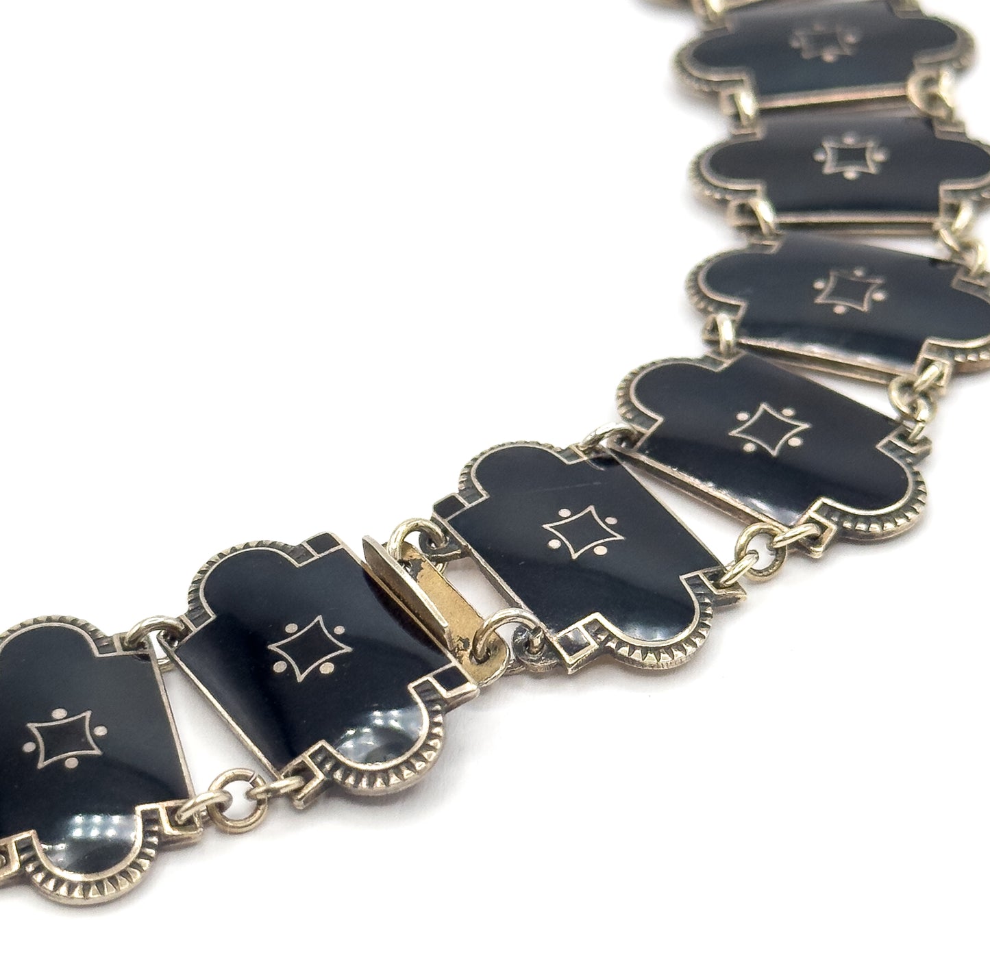 A diagonal view along the front of the necklace, the black enamel links with their star motifs and scalloped silver borders receding into the distance, the clasp sitting mid-curve.