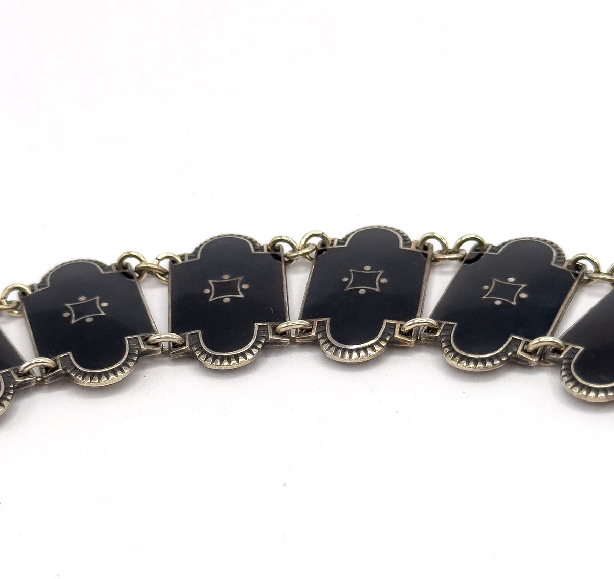 A tight close-up of five enamel links in a row, each showing the small four-pointed star with dots and the fan-like fluted edge along its lower border, joined by round jump rings.