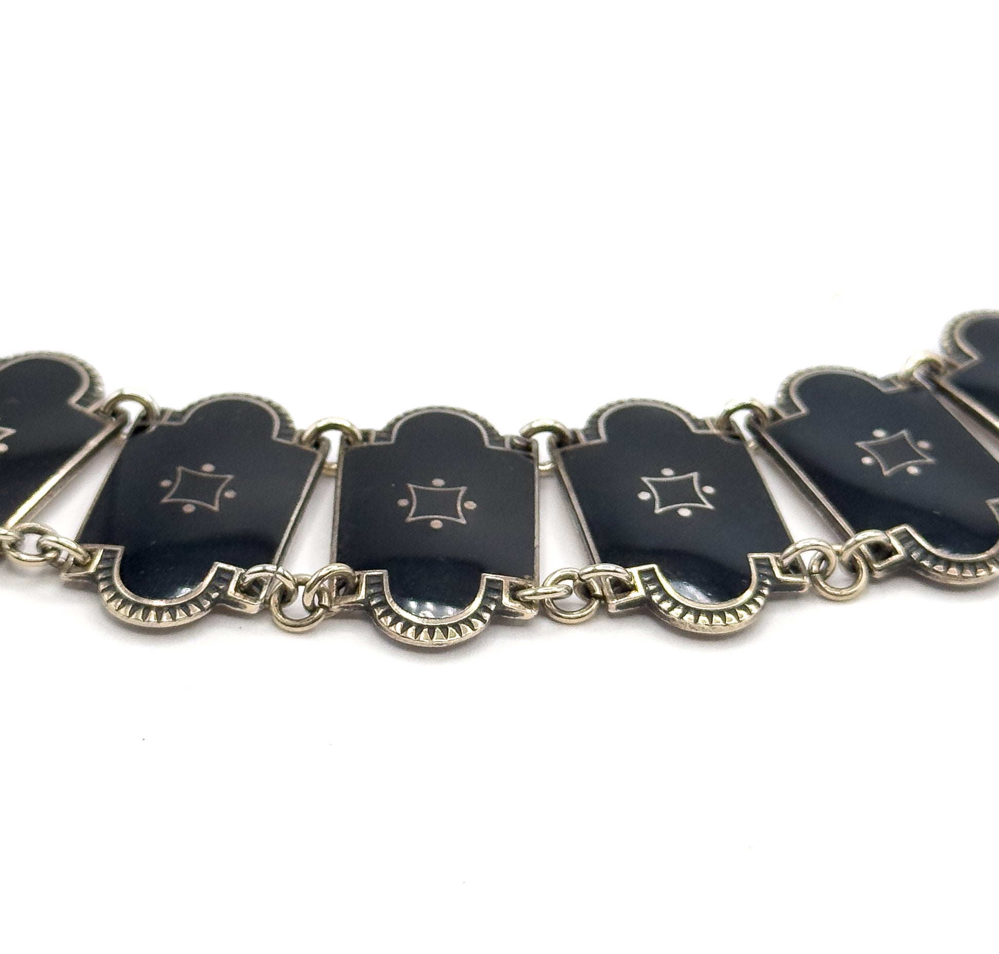 A shallow arc of the necklace seen from slightly below, the enamel links tipping at different angles on their double jump rings so the fluted silver undersides and link edges show.
