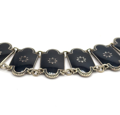 A shallow arc of the necklace seen from slightly below, the enamel links tipping at different angles on their double jump rings so the fluted silver undersides and link edges show.