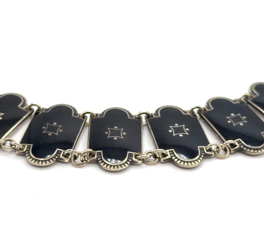 A shallow arc of the necklace seen from slightly below, the enamel links tipping at different angles on their double jump rings so the fluted silver undersides and link edges show.