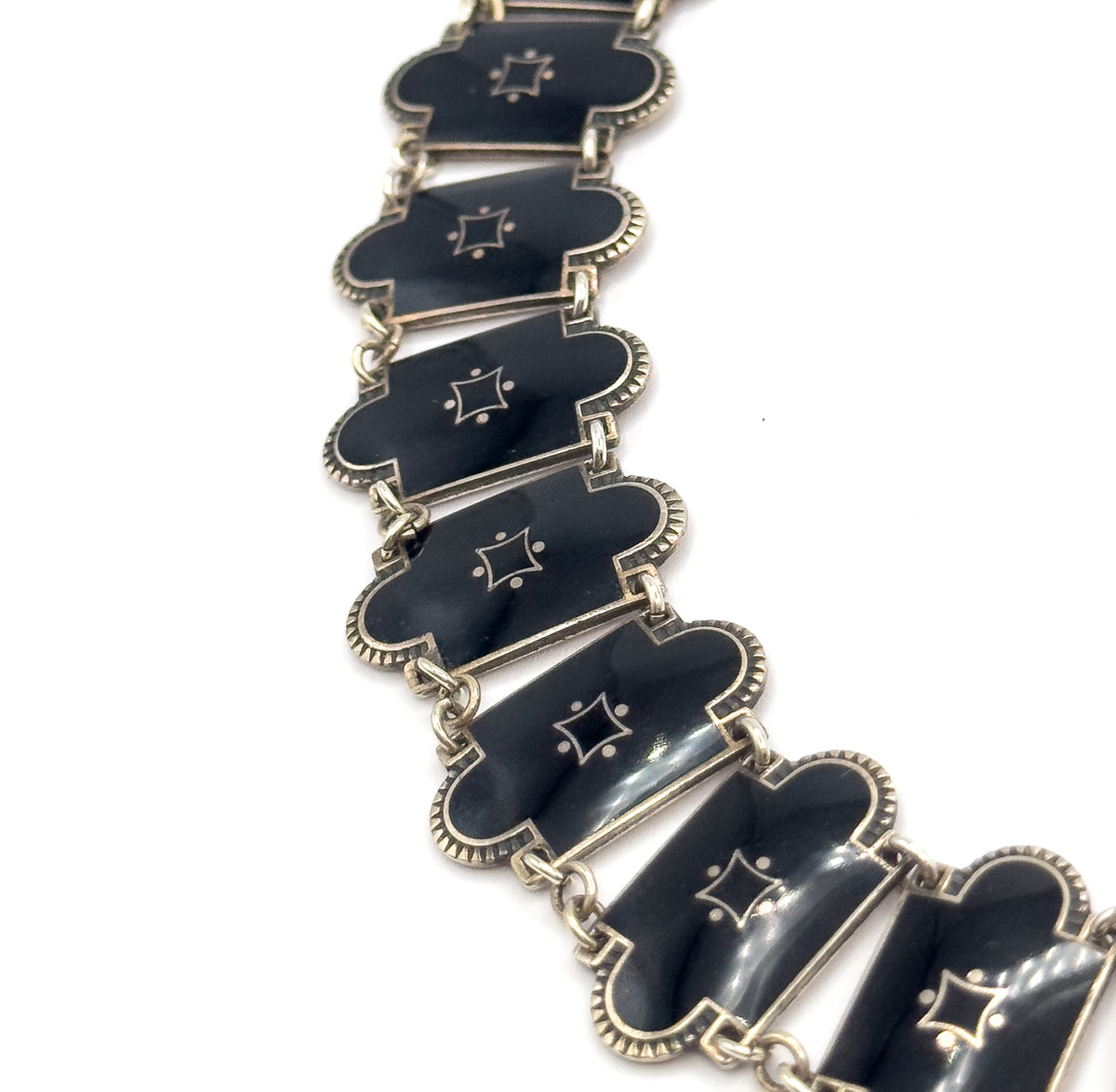 A steep overhead diagonal of the link chain running corner to corner, each black enamel station catching a bright highlight along its curved face beside the four-pointed star.