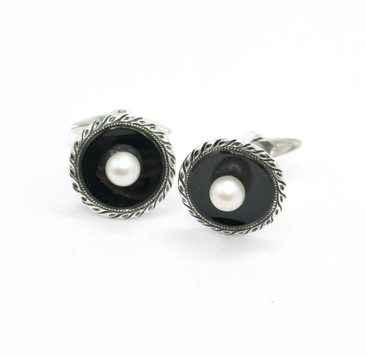 Art Deco faux onyx and pearl cufflinks in sterling silver, the pair shown face up on a plain white background, etched leafy borders framing black glass with a central pearl, one swivel bar visible.