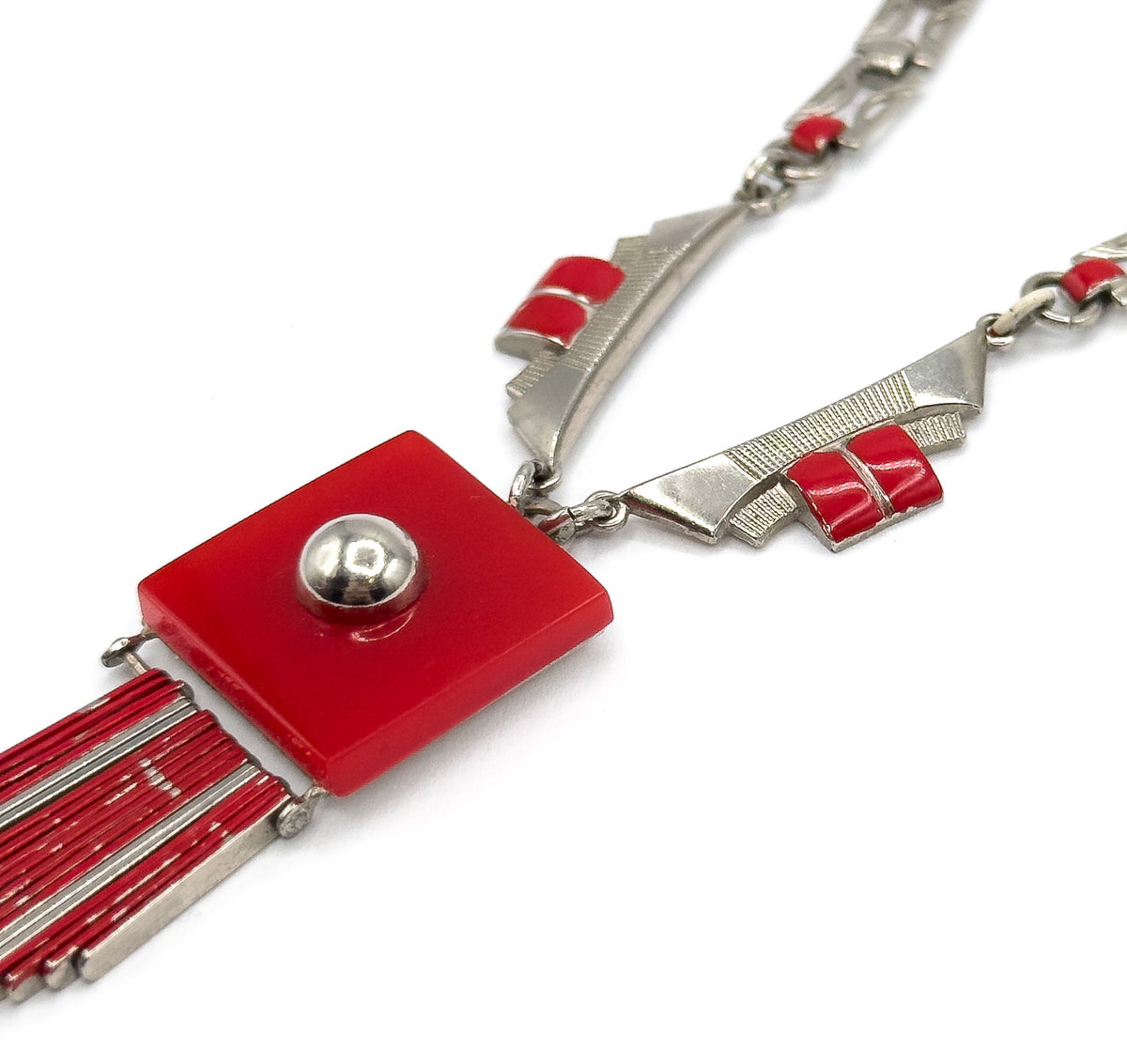 Angled three-quarter view showing the thickness of the red square plaque and its domed stud, with the chain's wedge-shaped links and paired red enamel bars sweeping off to the upper right.