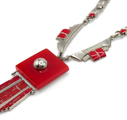 Angled three-quarter view showing the thickness of the red square plaque and its domed stud, with the chain's wedge-shaped links and paired red enamel bars sweeping off to the upper right.