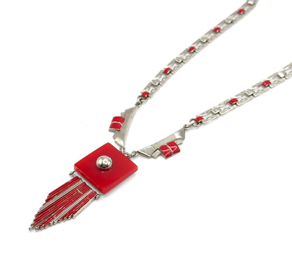 The whole necklace laid diagonally on white, chain receding to the upper right past the angled shoulder links with red bars, while the red square plaque and its fanned fringe rods point to the lower left.