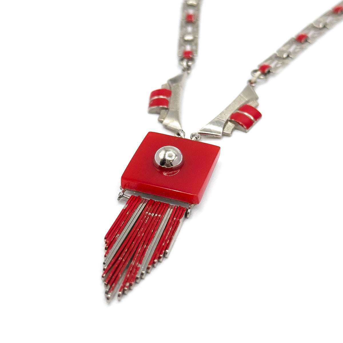 Tilted overhead view with both sides of the chain running up to the top corners, the red square plaque and its domed stud facing the camera and the fringe rods fanning diagonally to the lower left.