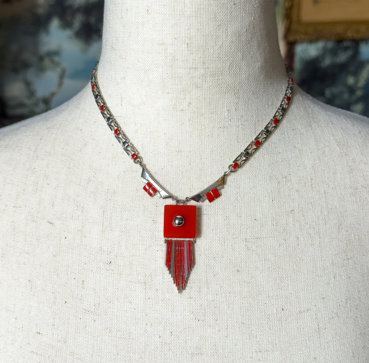 Art Deco enamel fringe necklace in base metal, shown at the neck on a linen bust form, its orangish red plastic square centre dropping a row of swaying fringe links.