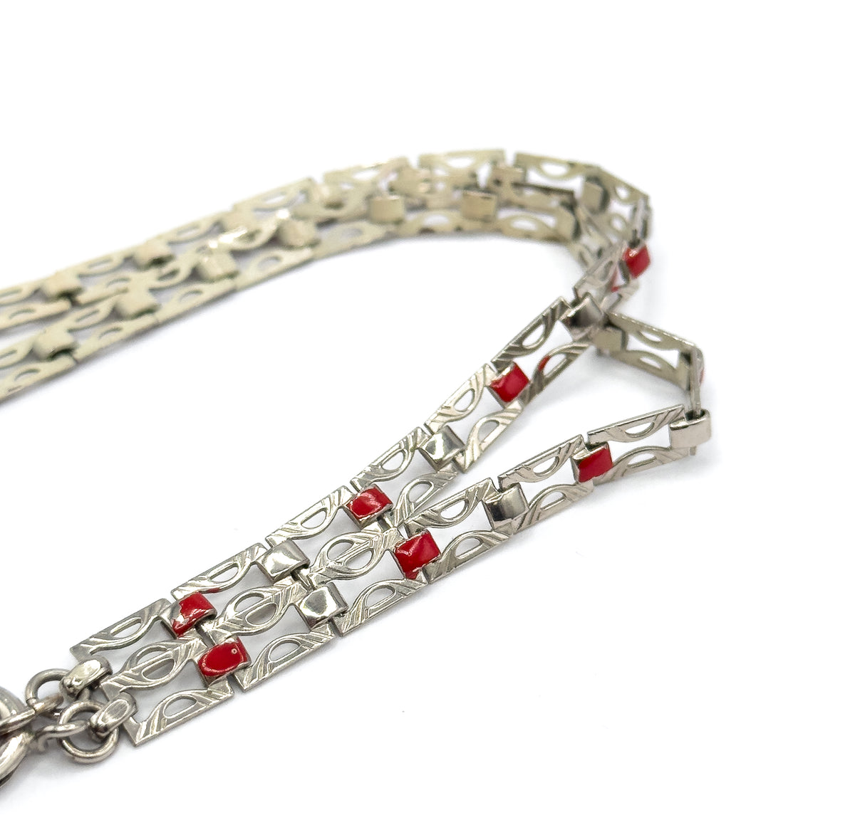 Laid on a white surface, the chain curves back on itself to show the pierced openwork links, their small red enamel squares, and a ring clasp at the lower edge.