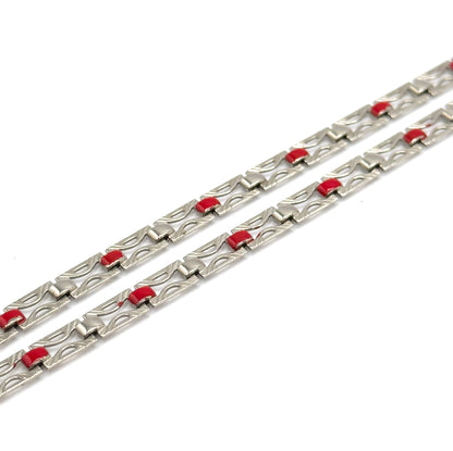 Two diagonal runs of chain fill the frame, lit so the engraved lines inside each pierced link stand out and the red enamel squares repeat evenly along both lengths.