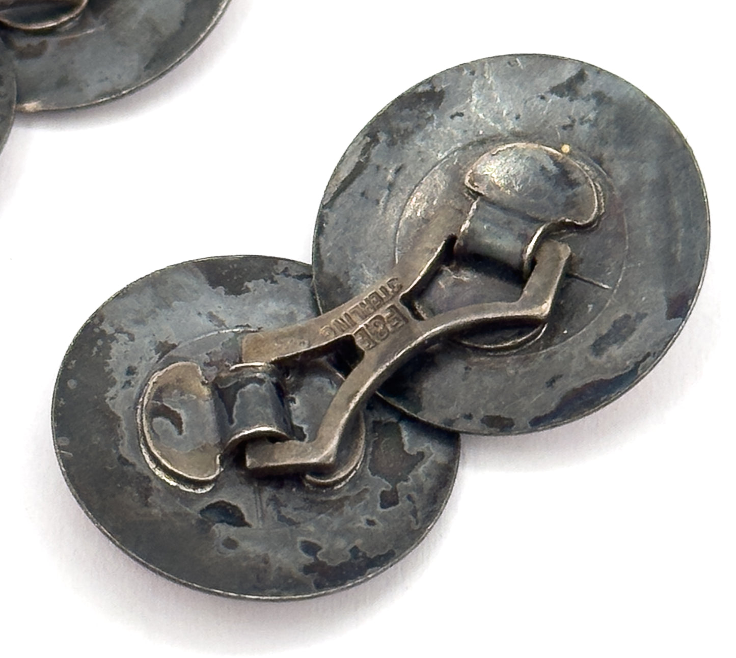 Close-up of the reverse, showing the curved link bar joining the two discs and the stamped lettering along it, the silver darkened with patina.