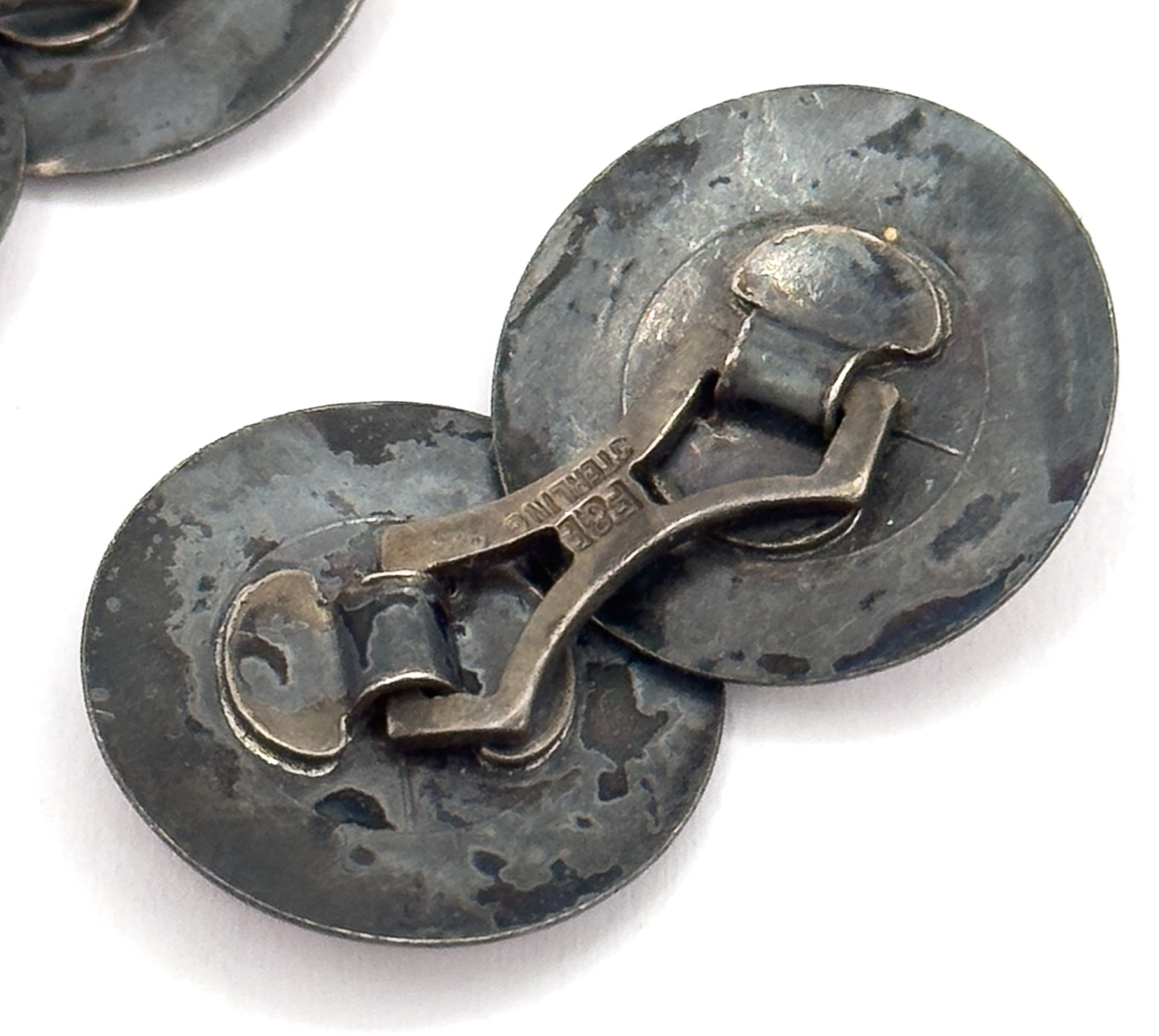 Close-up of the reverse, showing the curved link bar joining the two discs and the stamped lettering along it, the silver darkened with patina.