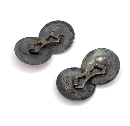 Both cufflinks are seen from behind together, their hinged link bars and darkened patinated backs facing up, one pair angled above the other.