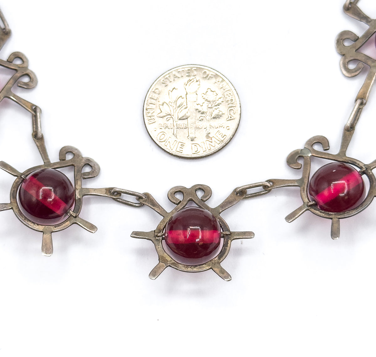 A dime rests beside three atomic insect stations for scale, each sterling motif with curled antennae and radiating legs holding a round cranberry glass bead between elongated links.
