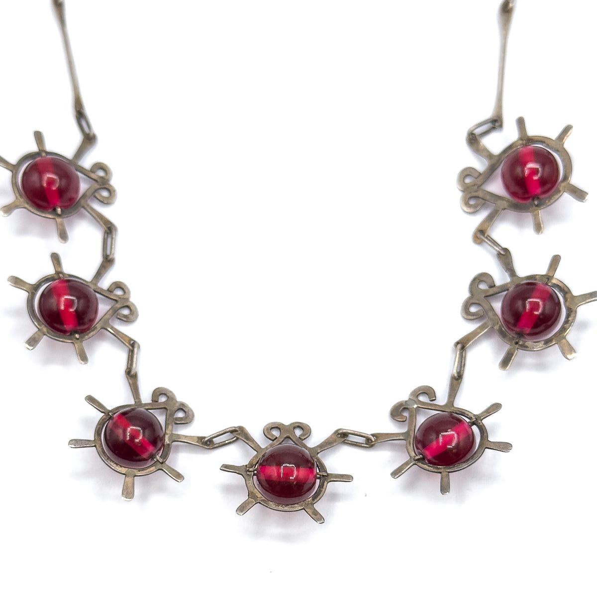 Seven atomic insect stations curve across the frame in the necklace's front section, their cranberry glass beads and radiating sterling legs joined by elongated links on white.