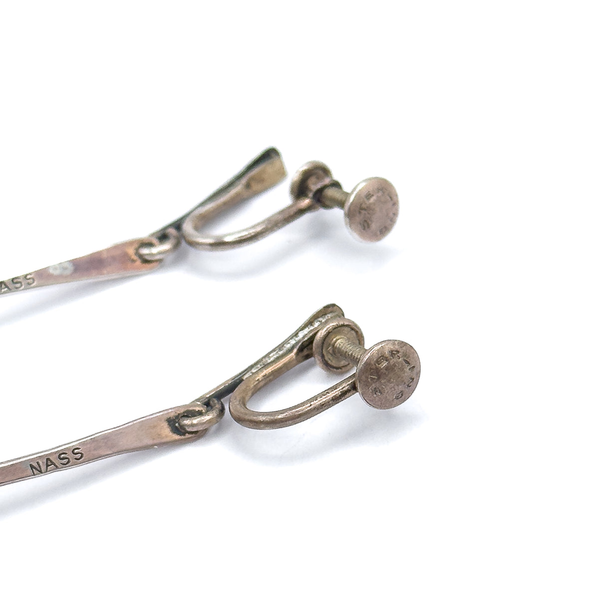 Close-up of both earrings' screwback findings, the horseshoe wires and disc-tipped screws attached to flat sterling drops, one stamped "NASS".