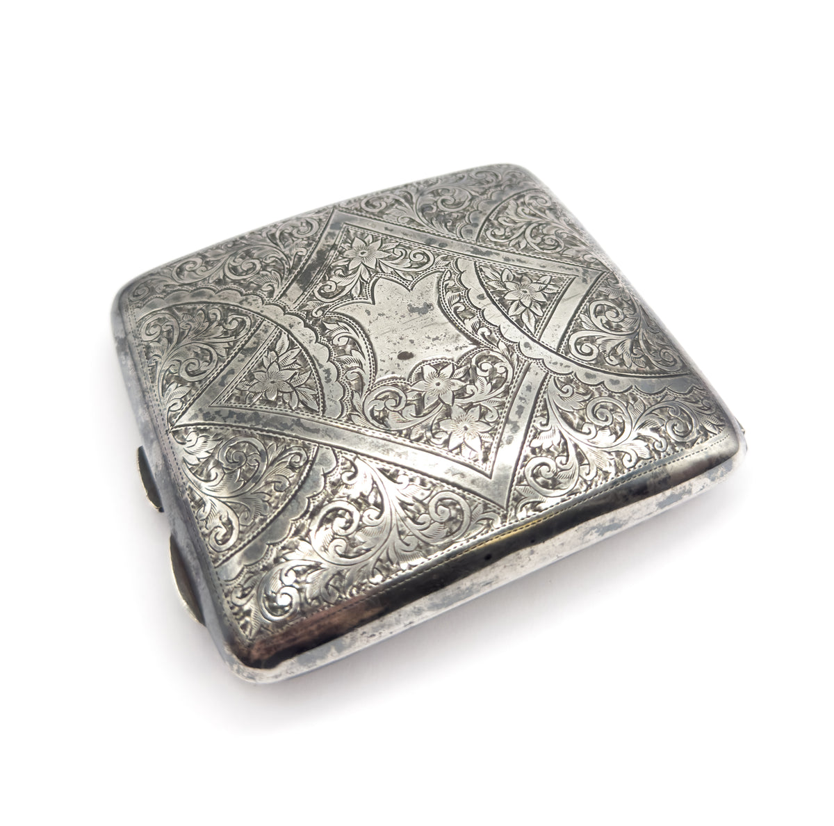 The closed silver case seen from above at an angle, the whole engraved lid in frame with scrolling foliage and small flowers around a plain centre panel.