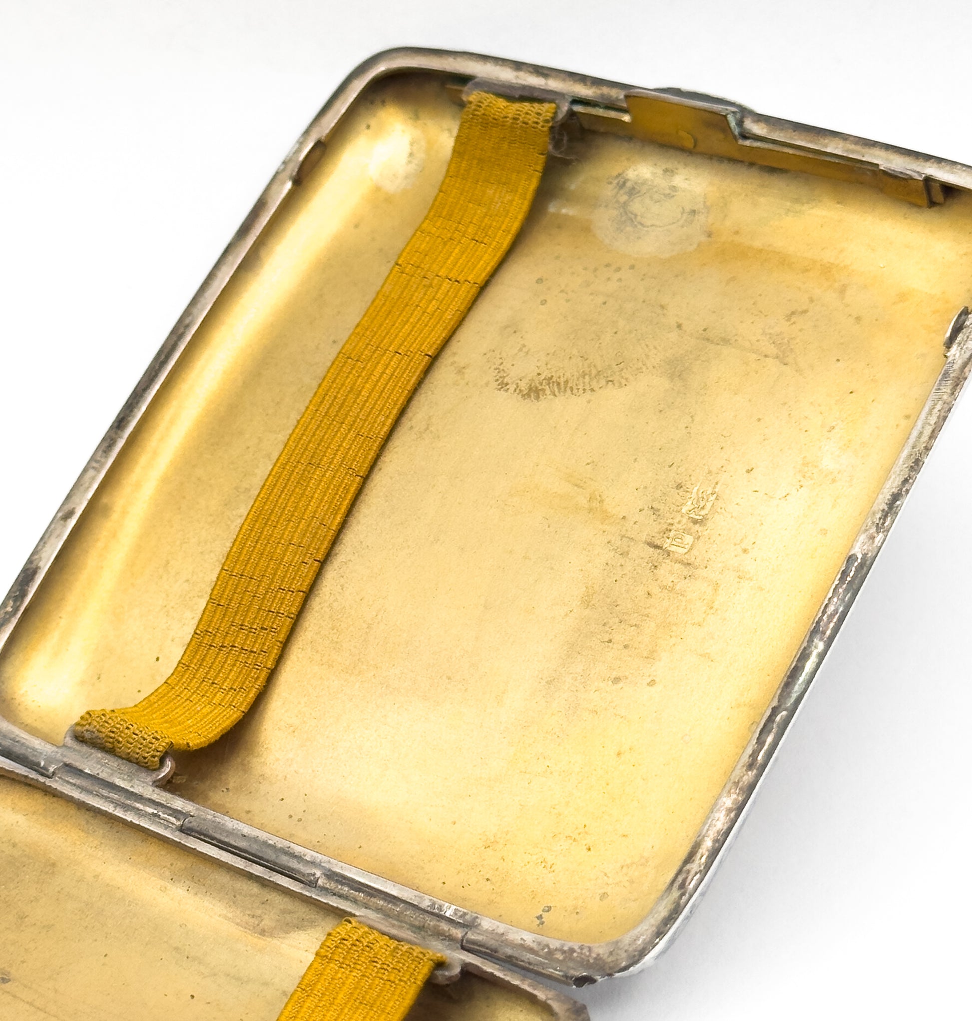 A close view inside one half of the case, the gilt surface catching the light, with the yellow strap anchored at each end.