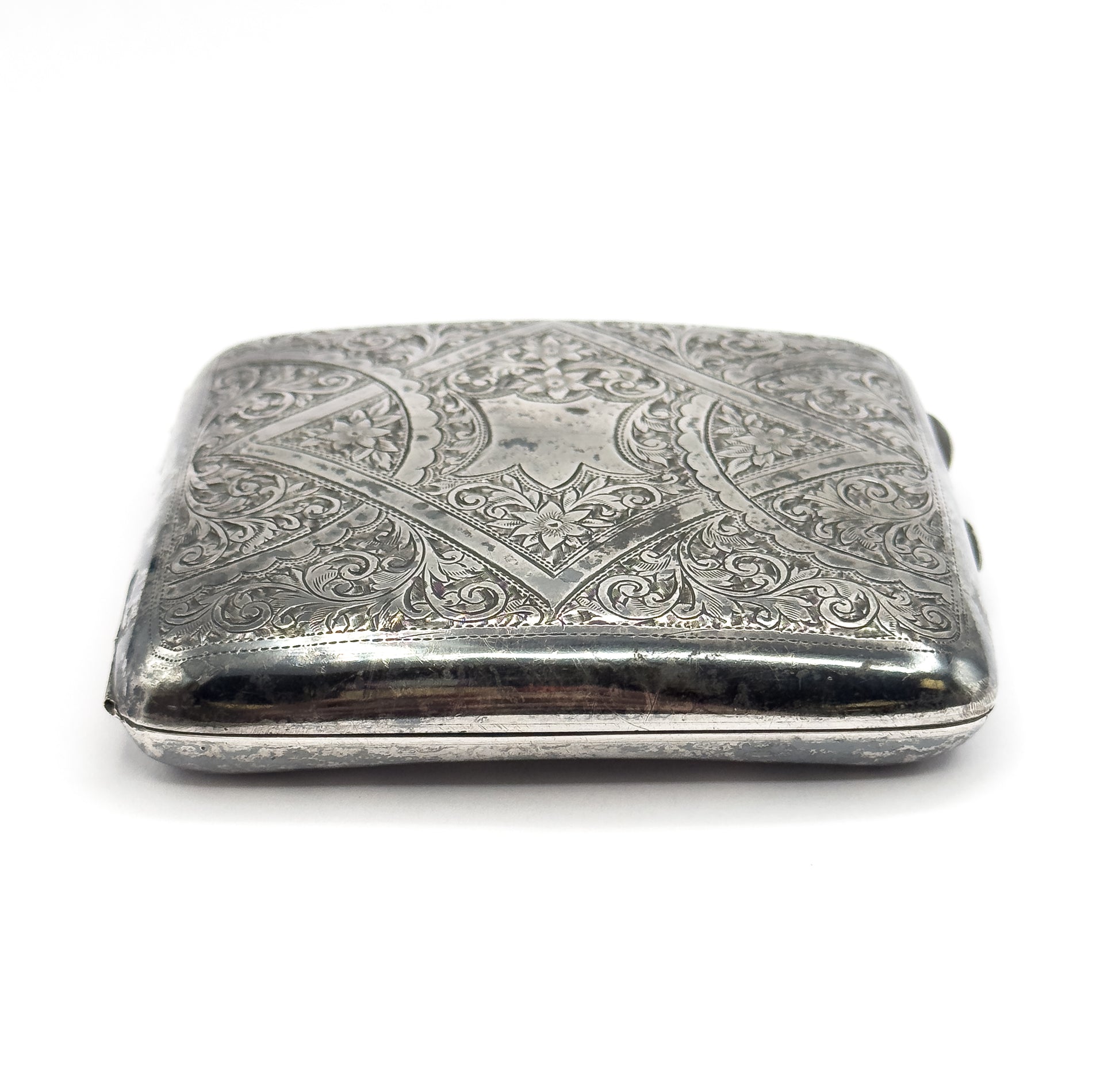 The case viewed end-on, showing its depth and the plain rounded side wall beneath the engraved lid, with darker patina along the rim.