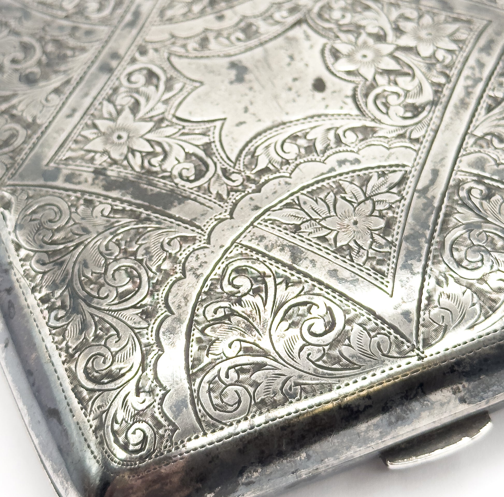 A close crop of one engraved corner, filling the frame with scrolling foliage, small flowers, and the fine stippled shading worked between them.