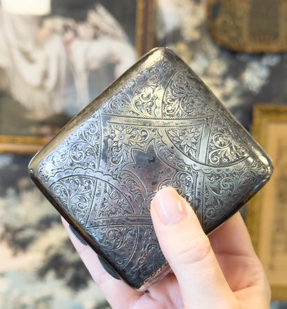 The case held in a hand and tipped corner-up, giving a sense of scale against the fingers, with framed pictures blurred in the background.