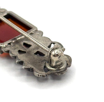 The reverse of the brooch in close-up, showing the pin stem crossing openwork sterling silver to a rounded catch, with a stamped mark on the darkened metal.