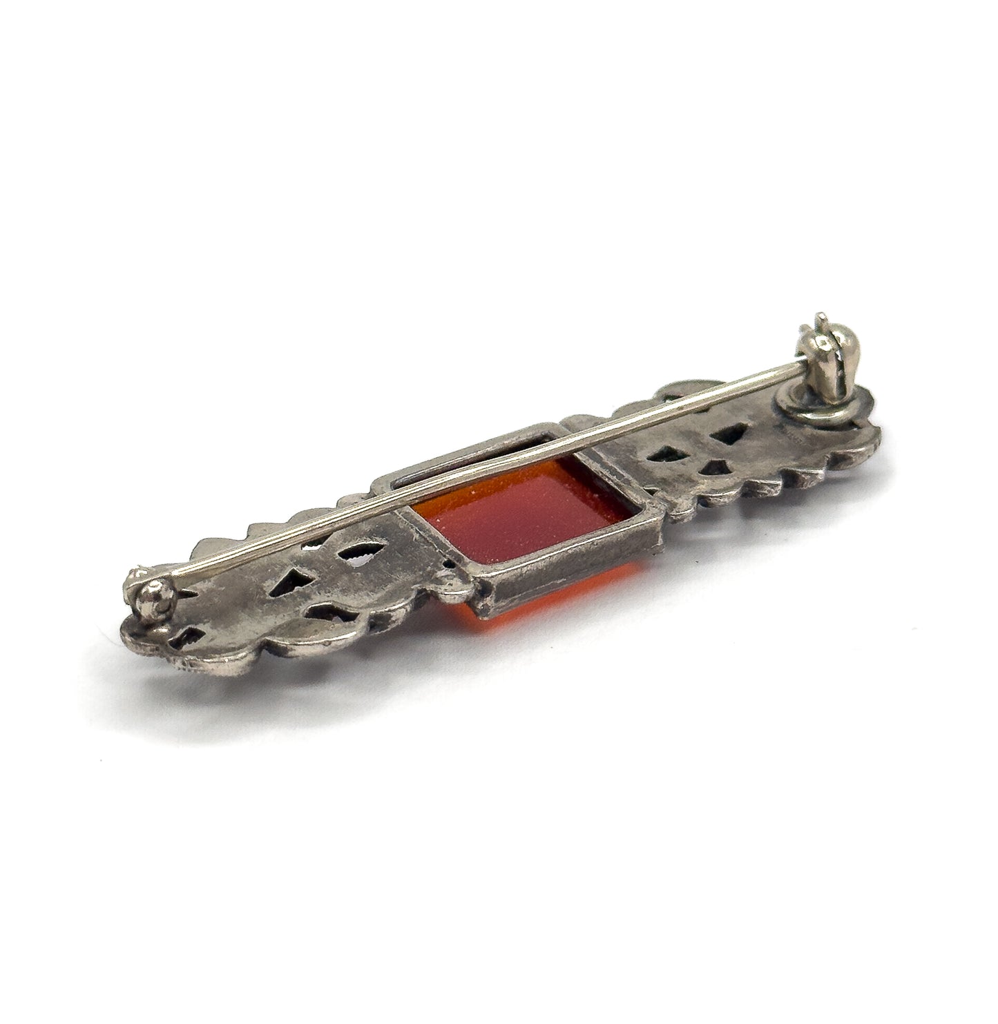 The reverse seen at an angle from one end, the pin stem lying along openwork silver with the carnelian's orange square visible through the back of its bezel.