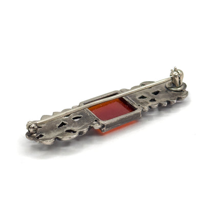 The reverse seen at an angle from one end, the pin stem lying along openwork silver with the carnelian's orange square visible through the back of its bezel.