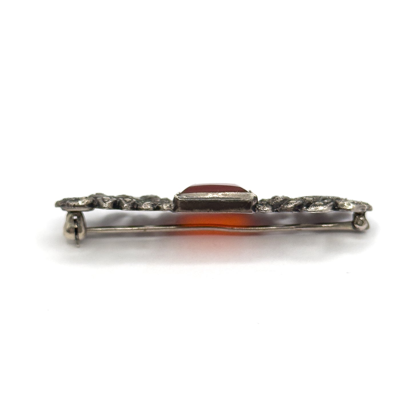 Edge-on profile view along the bar, the raised rectangular bezel standing above the marcasite-set silver ends with the pin stem running below and orange light glowing through the stone.