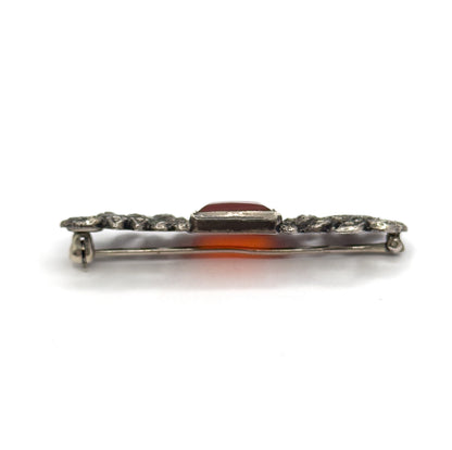 Edge-on profile view along the bar, the raised rectangular bezel standing above the marcasite-set silver ends with the pin stem running below and orange light glowing through the stone.