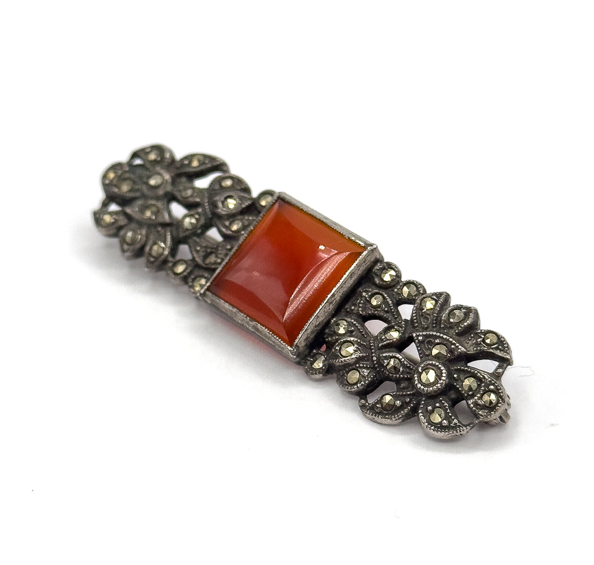 Angled three-quarter view from above the face, the square carnelian's bezel walls catching light while the darkened floral openwork ends recede, marcasites glinting across each petal.