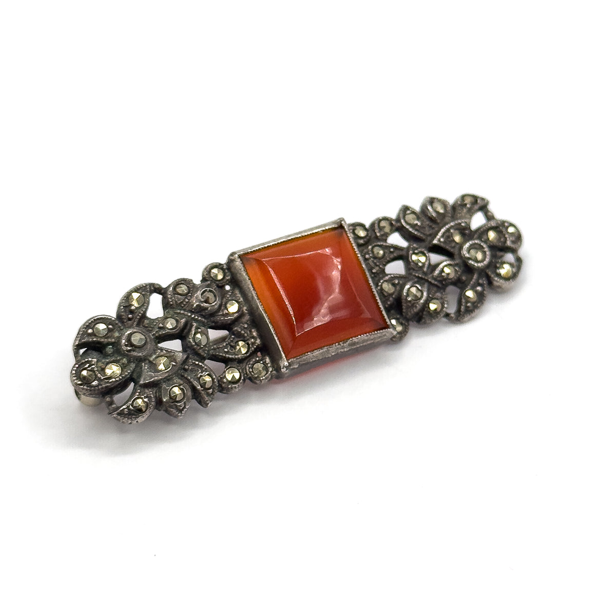The bar set diagonally across white, the carnelian's table-cut facets showing a soft highlight while the darkened silver flowerheads at each end sit almost flat to the camera.