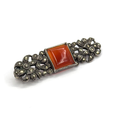 The bar set diagonally across white, the carnelian's table-cut facets showing a soft highlight while the darkened silver flowerheads at each end sit almost flat to the camera.