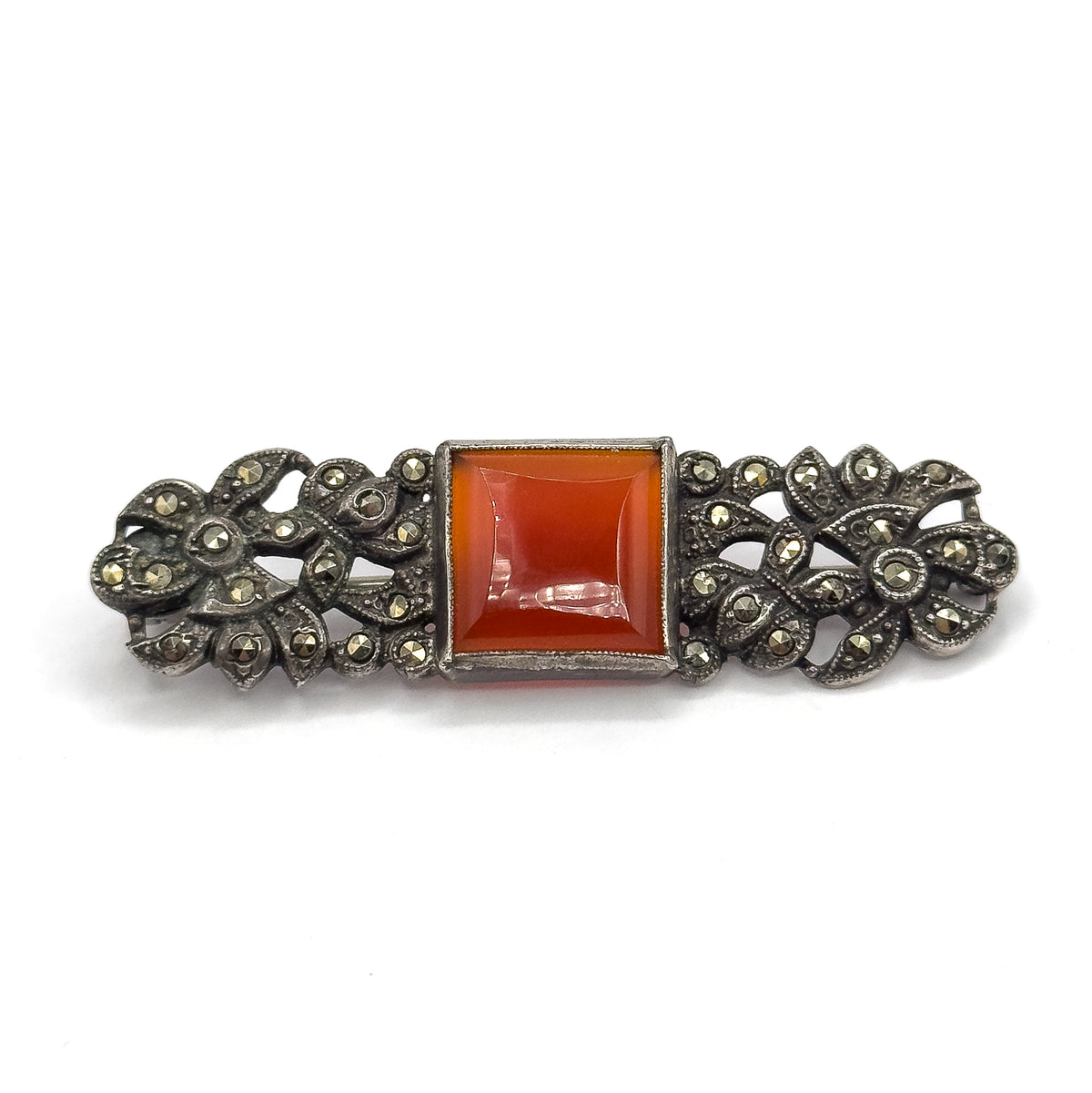 Straight-on face-up view horizontally across plain white, showing the full symmetry of the bar with the square carnelian bezel dead centre and matching marcasite flowerheads at each end.