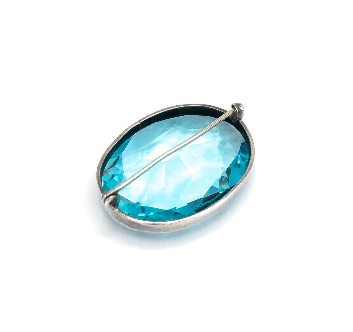 Reverse view on white, the open-back sterling silver bezel letting light through the blue paste stone, with the pin stem crossing the back and the C clasp at the upper edge.
