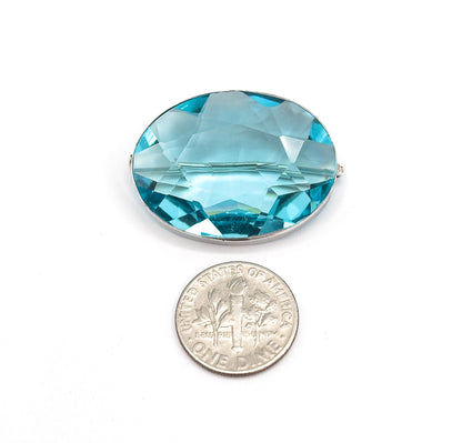 The brooch lies face up on white beside a dime, the coin roughly two-thirds the height of the oval paste stone, with the sterling silver bezel and pin catch just visible at the sides.