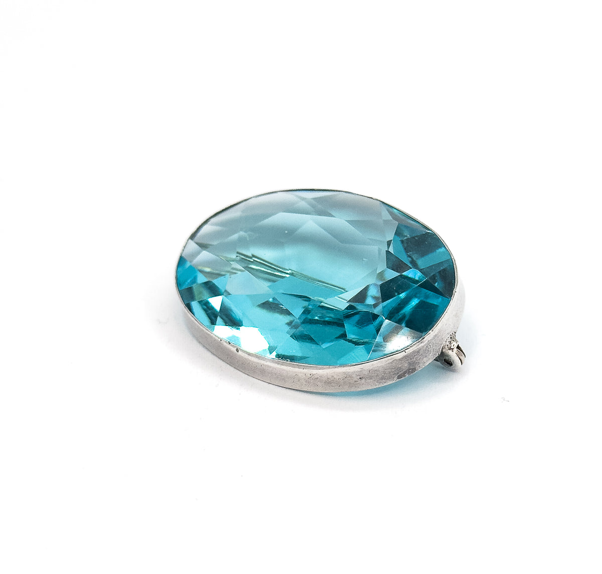 A raised three-quarter view on white, looking down across the faceted table of the blue paste stone so the light-catching facets and the smooth sterling silver bezel rim both show, C clasp at the right.