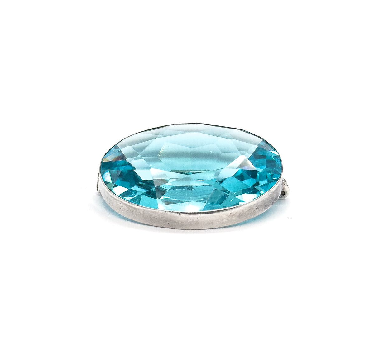 Low, near eye-level three-quarter view on white, the oval foreshortened so the faceted stone flashes across its width above the smooth sterling silver bezel wall, hinge and clasp nubs at each side.