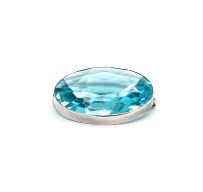 Low, near eye-level three-quarter view on white, the oval foreshortened so the faceted stone flashes across its width above the smooth sterling silver bezel wall, hinge and clasp nubs at each side.