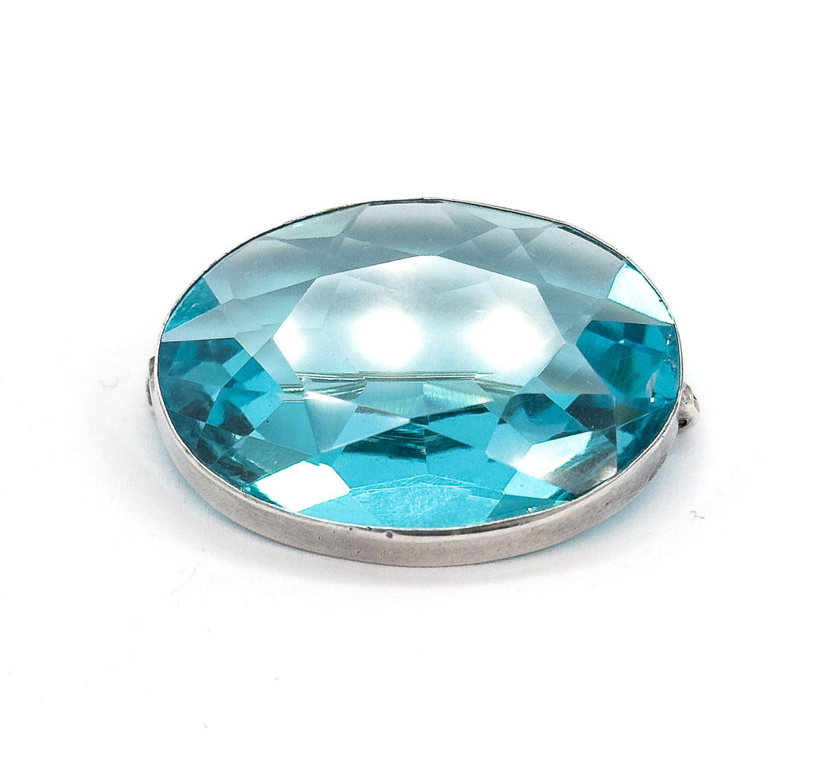 Tilted view on white with the oval leaning back, bright highlights pooling across the centre of the blue paste stone while the sterling silver bezel band curves along the lower edge.