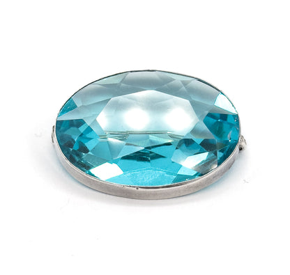 Tilted view on white with the oval leaning back, bright highlights pooling across the centre of the blue paste stone while the sterling silver bezel band curves along the lower edge.