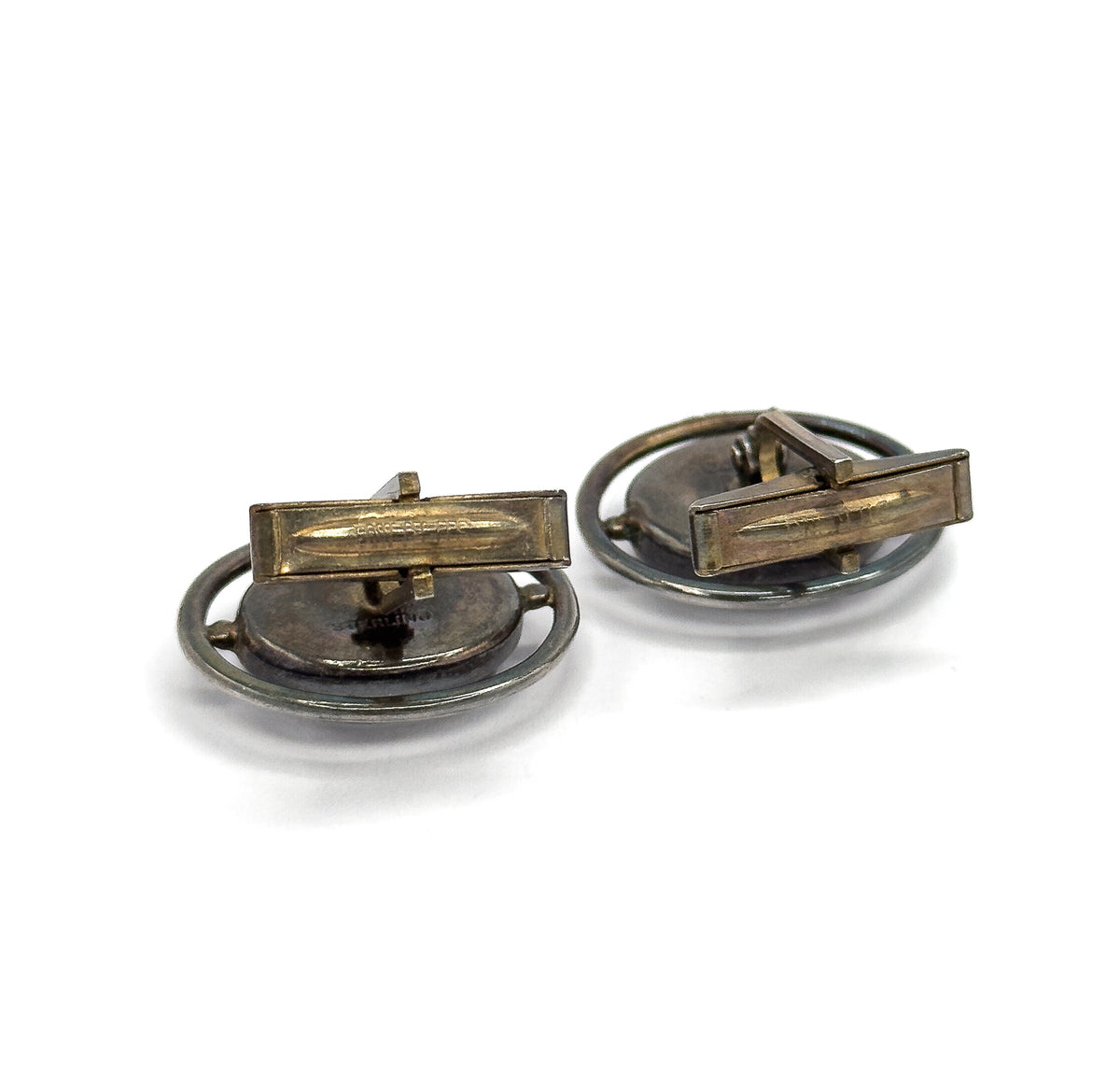 Reverse view of the pair with both toggle bars swung across the backs of the oval faces, where small stamped marks are visible on the darkened silver.