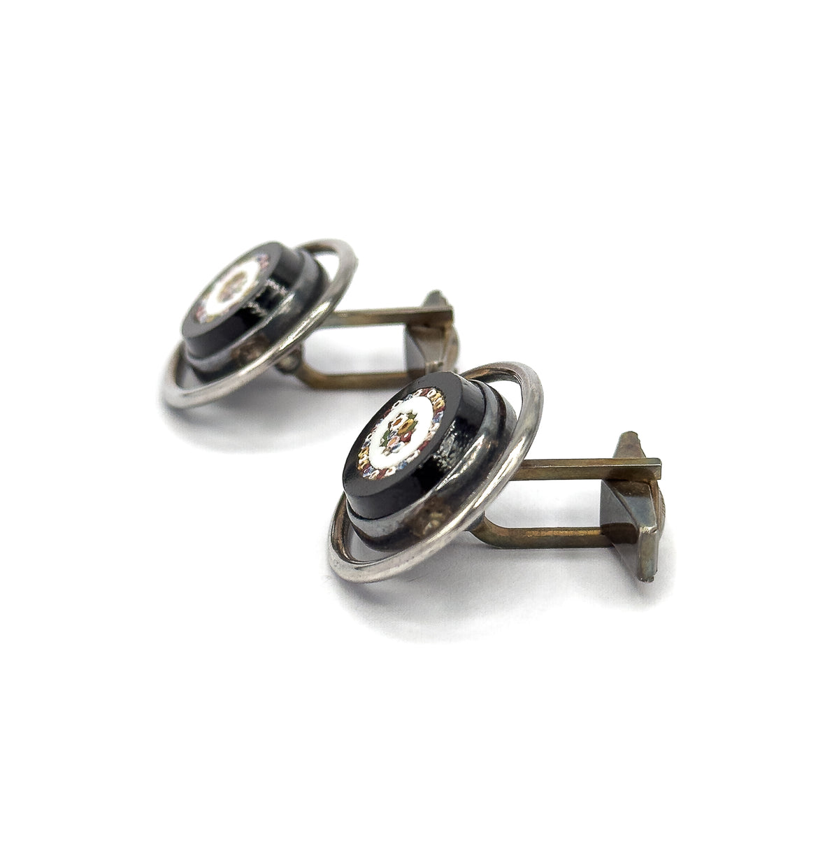 Steep side-on view of both cufflinks angled together, showing the raised domed profile of each mosaic oval sitting within its silver hoop, with the toggle bars trailing off to one side.