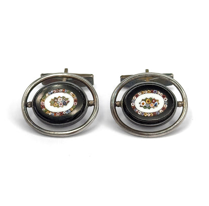 Straight-on front view of the pair side by side, each dark oval face showing its glass mosaic flower ringed by tiny multicoloured tesserae, with the toggle bars visible behind the silver hoops.
